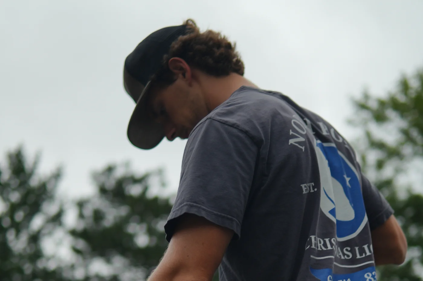 Looking up at an installer in a North Pole cap and shirt, head down over his work, the bear mark across his back against an overcast sky