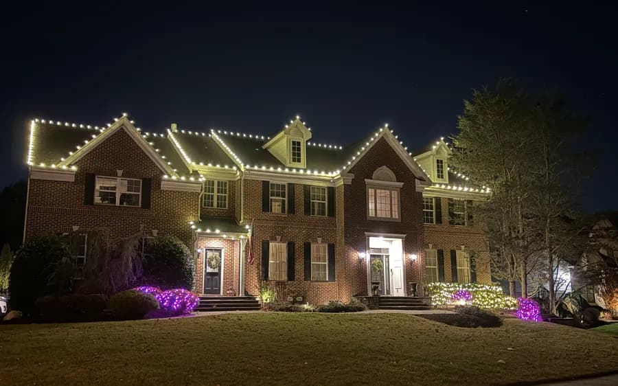 A brick colonial with every roofline run and the front trees lit
