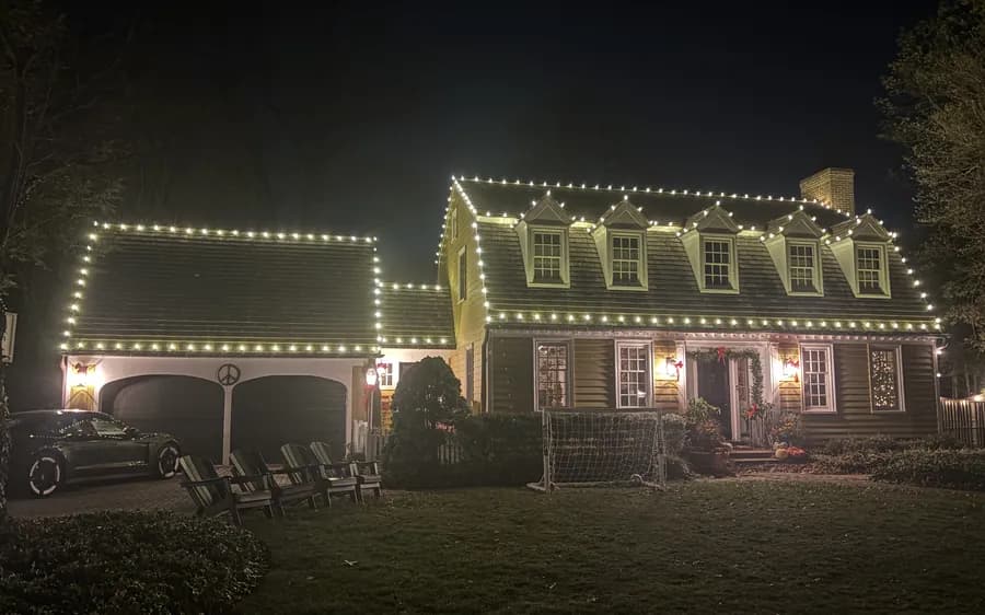 A cape with dormers picked out in warm white, lit shrubs along the front