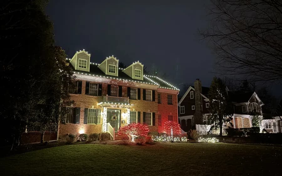 A colonial with warm white rooflines and red accent lighting at the foundation