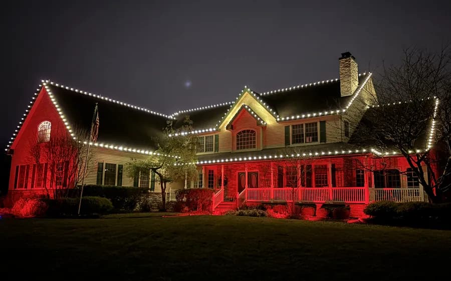 A long low home with warm rooflines and deep red uplighting across the facade