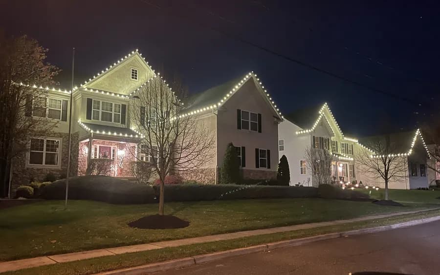 A wide home seen from the street with rooflines and a wrapped tree lit