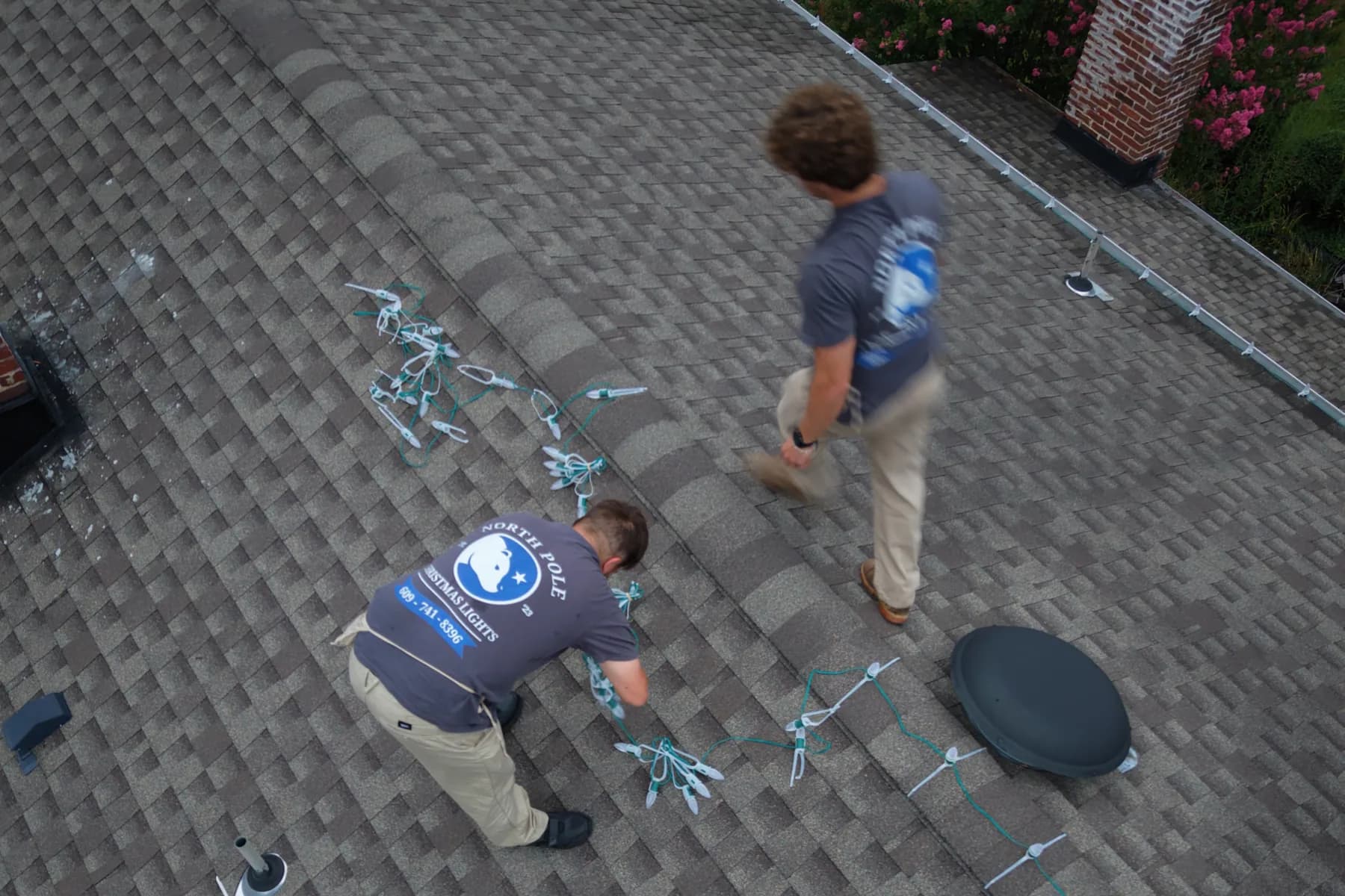 Two North Pole installers seen from above, running a strand of lights along the ridge