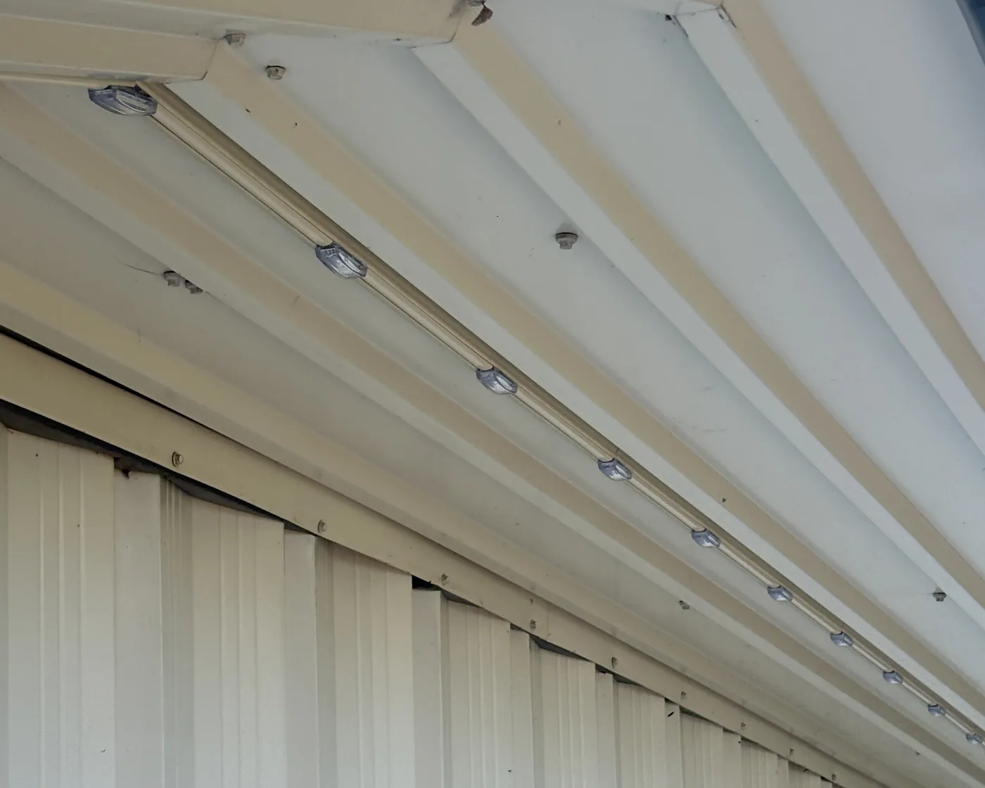 A permanent lighting track running under a soffit in daylight, the light pods set into it at even spacing
