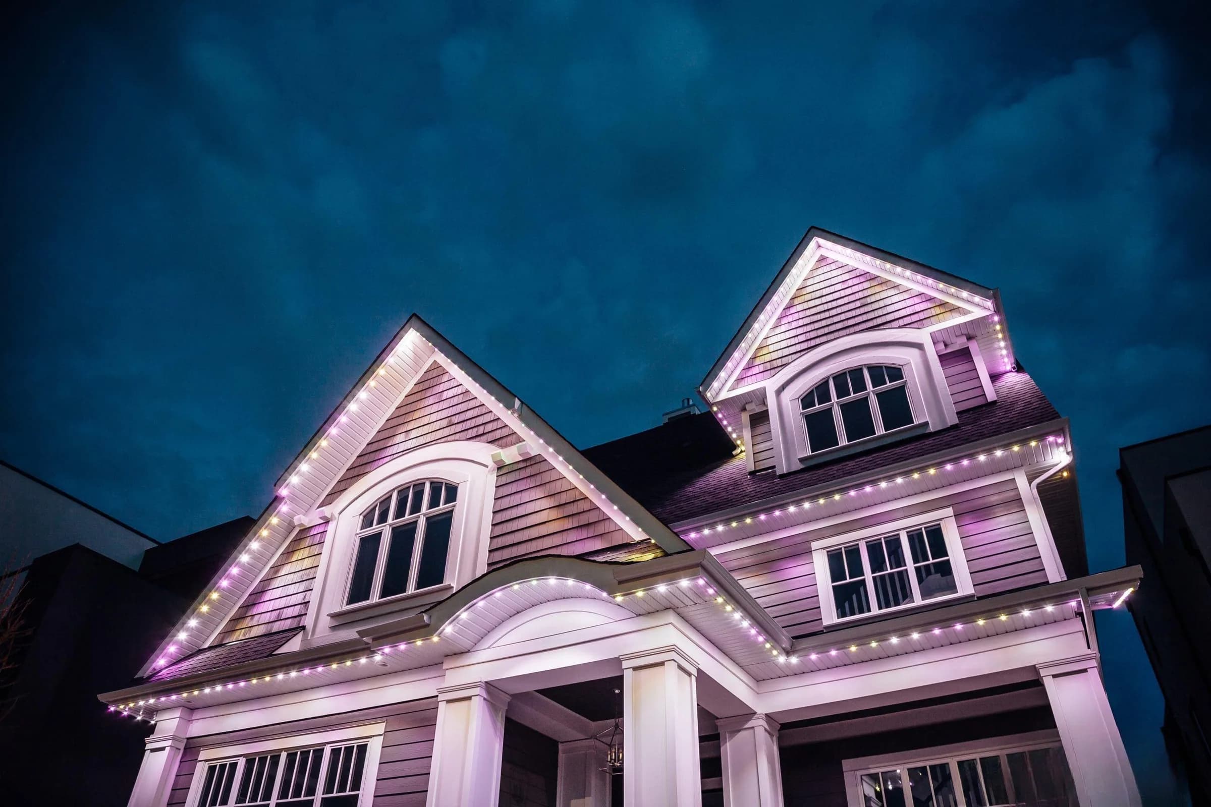 A house at night with permanent lighting in pink and warm white along every gable, dormer and eave