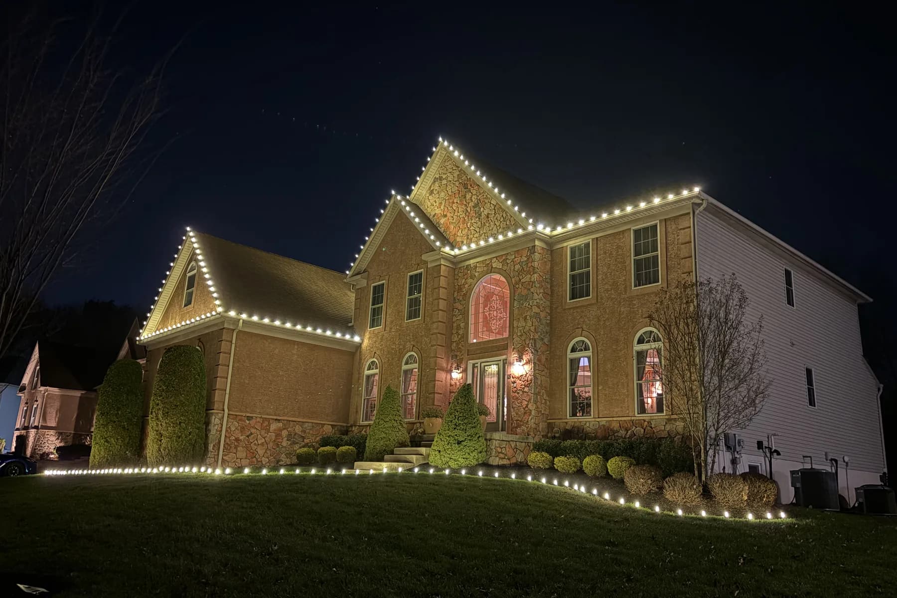 Warm white roofline lighting picked out along every eave, peak and gable of a large home