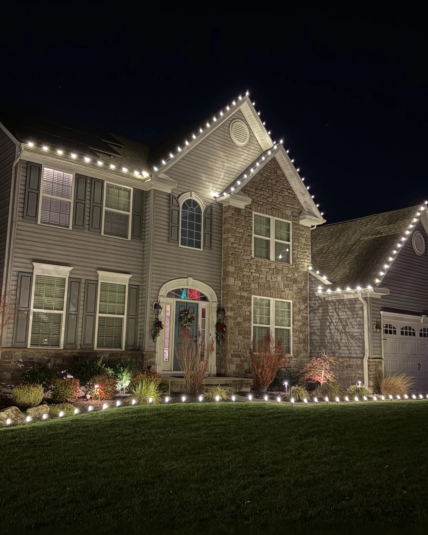 North Pole install: a two-story home with warm white rooflines and a lit garage bay